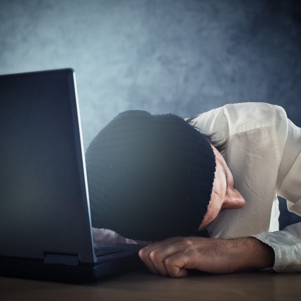 Exhausted man sleeps on laptop at office desk after working overtime.